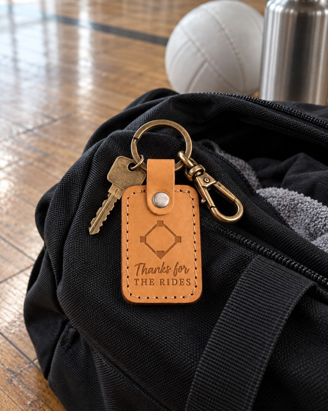 Golden brown Thanks for the Rides keychain on an open black duffel bag on a sunlit gym floor