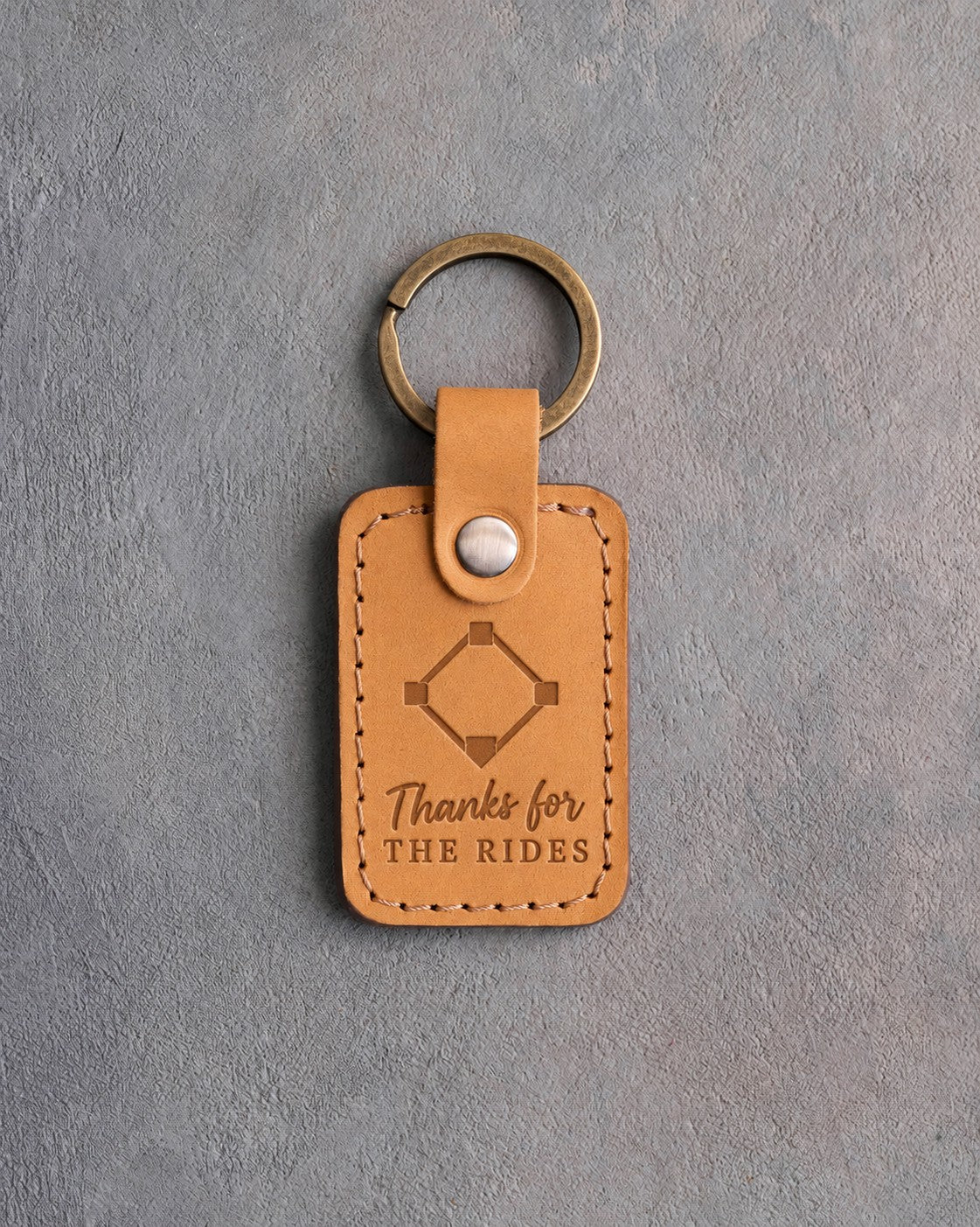 Golden brown leather keychain debossed with a baseball diamond and the words Thanks for THE RIDES, on gray plaster