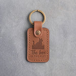 Caramel leather keychain debossed with a cat sitting in an open cardboard box above the words The box IS THE GIFT