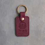 Sangria red leather keychain debossed with an egg basket above the words The girls ARE LAYING, on gray concrete