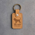 Indian Summer tan leather keychain debossed with a Bloodhound silhouette and the words The nose KNOWS, on gray concrete