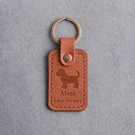 Caramel leather keychain debossed with a standing puppy above Meet and THE PUPPY, on gray concrete