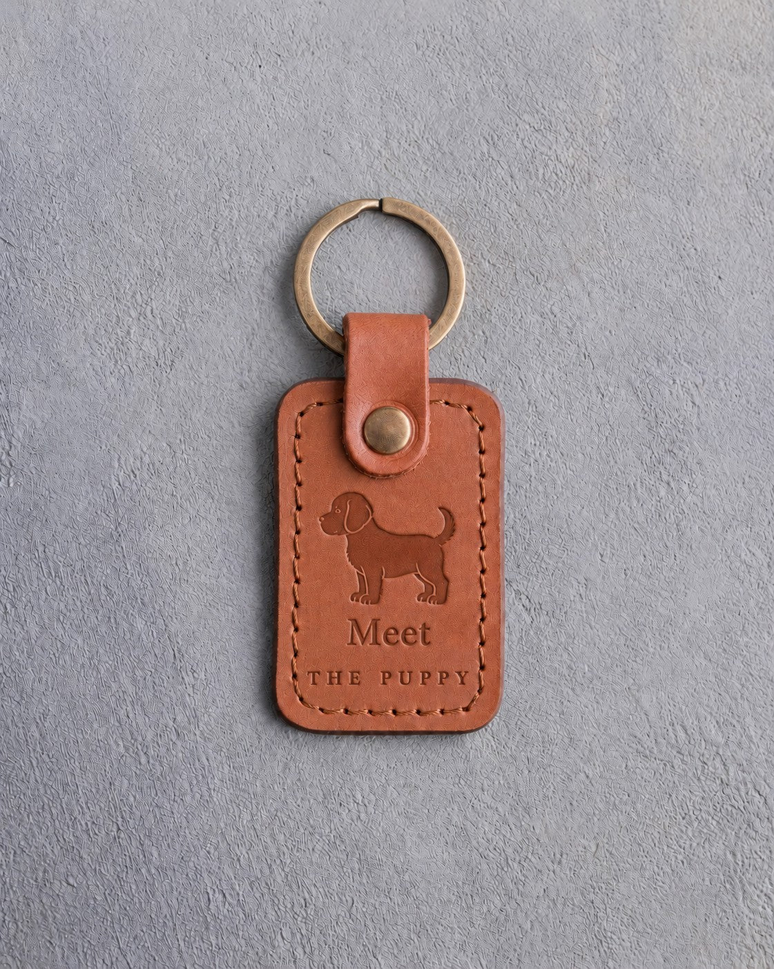 Caramel leather keychain debossed with a standing puppy above Meet and THE PUPPY, on gray concrete