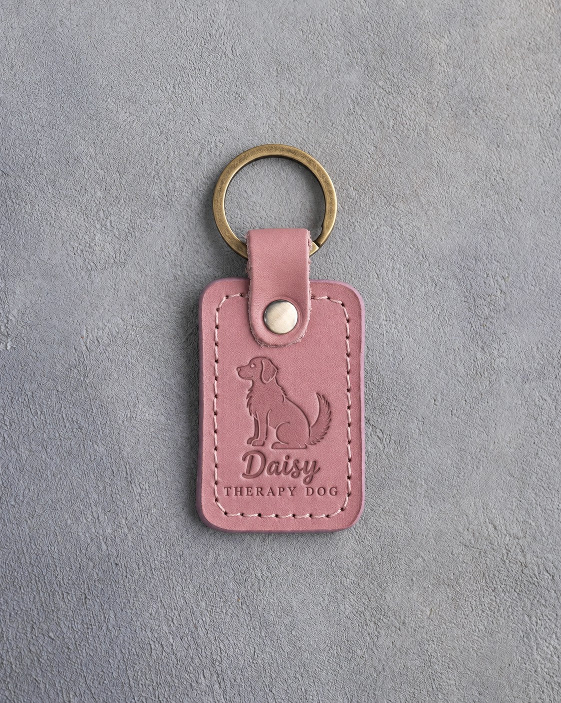 Parisian Blossom pink leather keychain debossed with a calm seated dog above Daisy and THERAPY DOG, on gray concrete