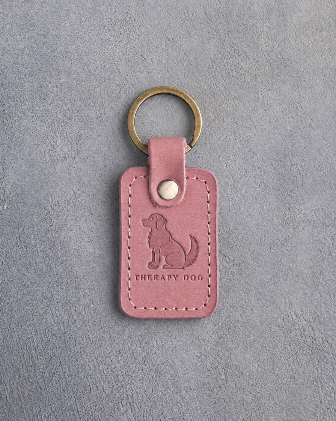 Parisian Blossom pink leather keychain debossed with a calm seated dog above THERAPY DOG, on gray concrete
