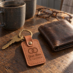 Year three IS LEATHER keychain in caramel leather on an oak kitchen table beside two stoneware mugs in morning sun