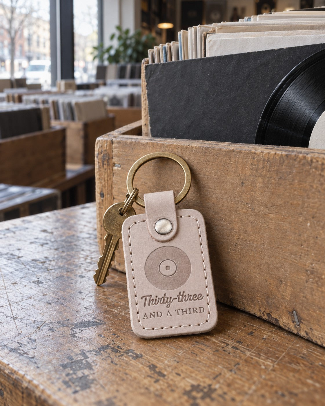 Thirty-Three and a Third keychain in soft gray leather beside a spinning turntable in a lamplit room