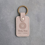 Gray sand leather keychain debossed with a vinyl record above the words Thirty-three AND A THIRD, on gray plaster