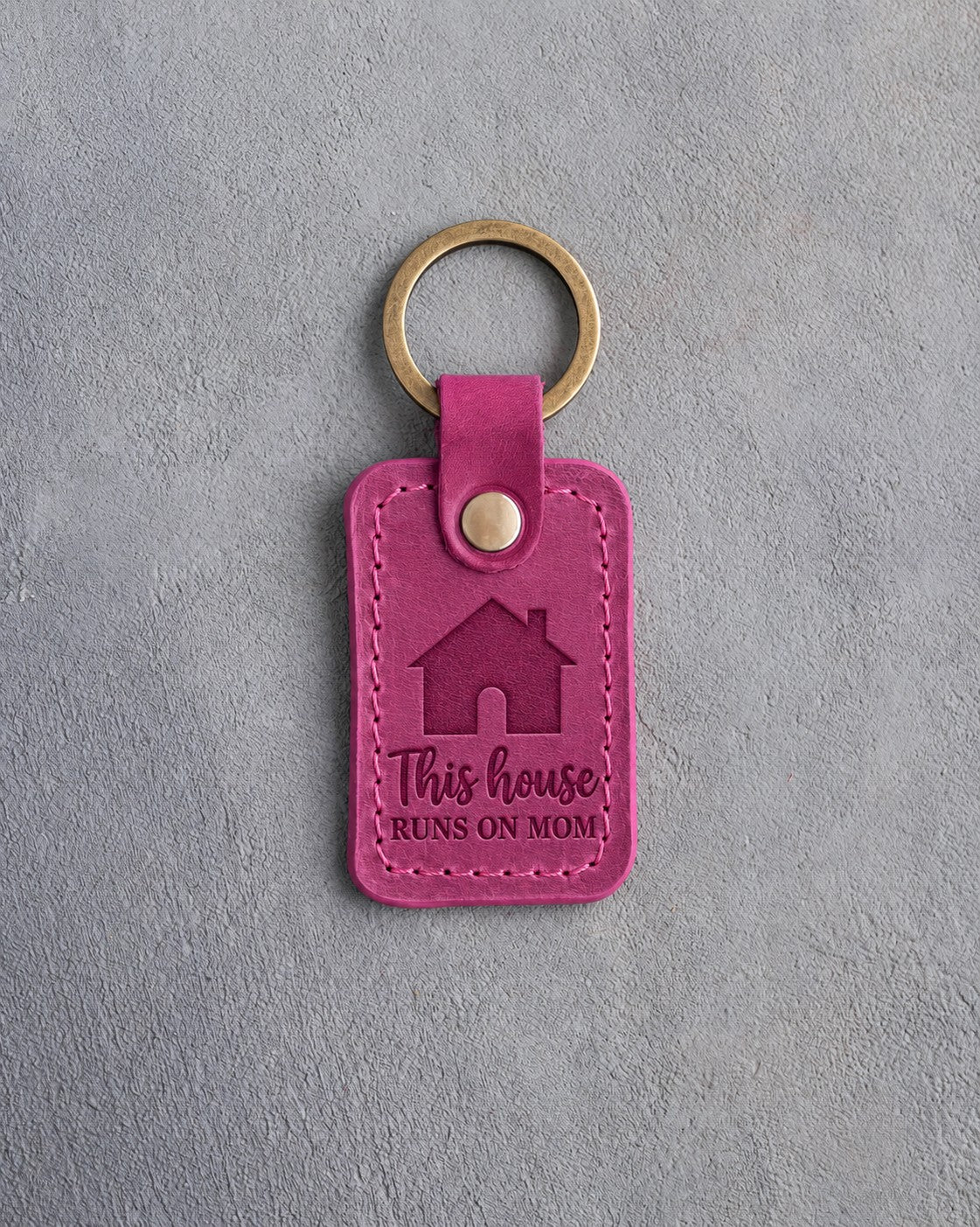 Fuchsia leather keychain debossed with a gabled house above This house and RUNS ON MOM