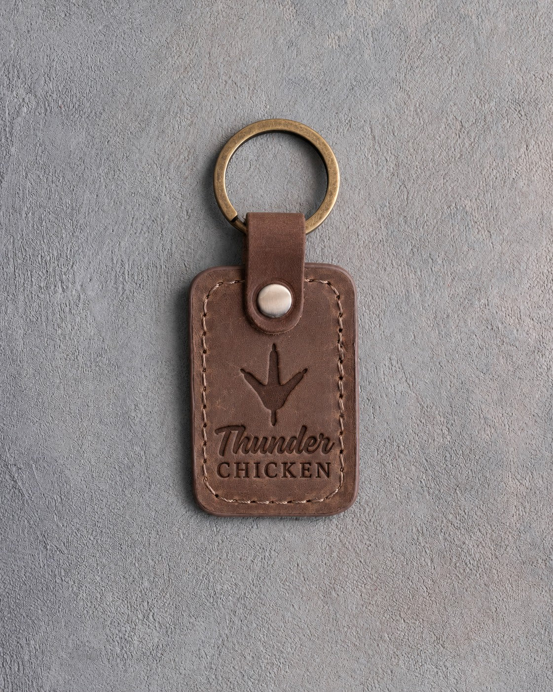 Sicilian brown leather keychain debossed with a wild turkey track above the words Thunder CHICKEN, on gray plaster