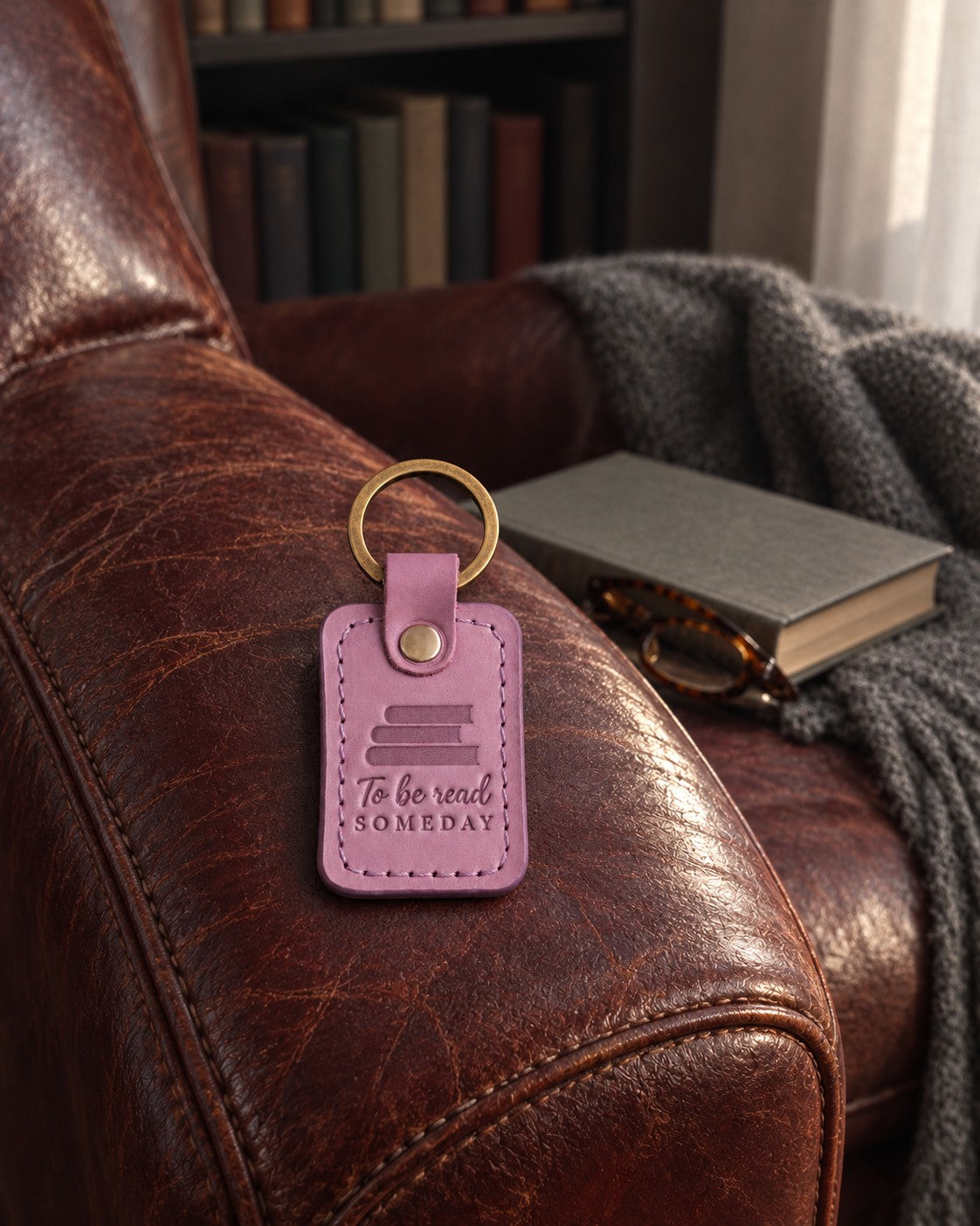 Lilac To be read SOMEDAY keychain on top of a tall stack of new books beside a bed