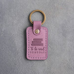 Lilac leather keychain debossed with a pile of three books above To be read and SOMEDAY, on gray concrete