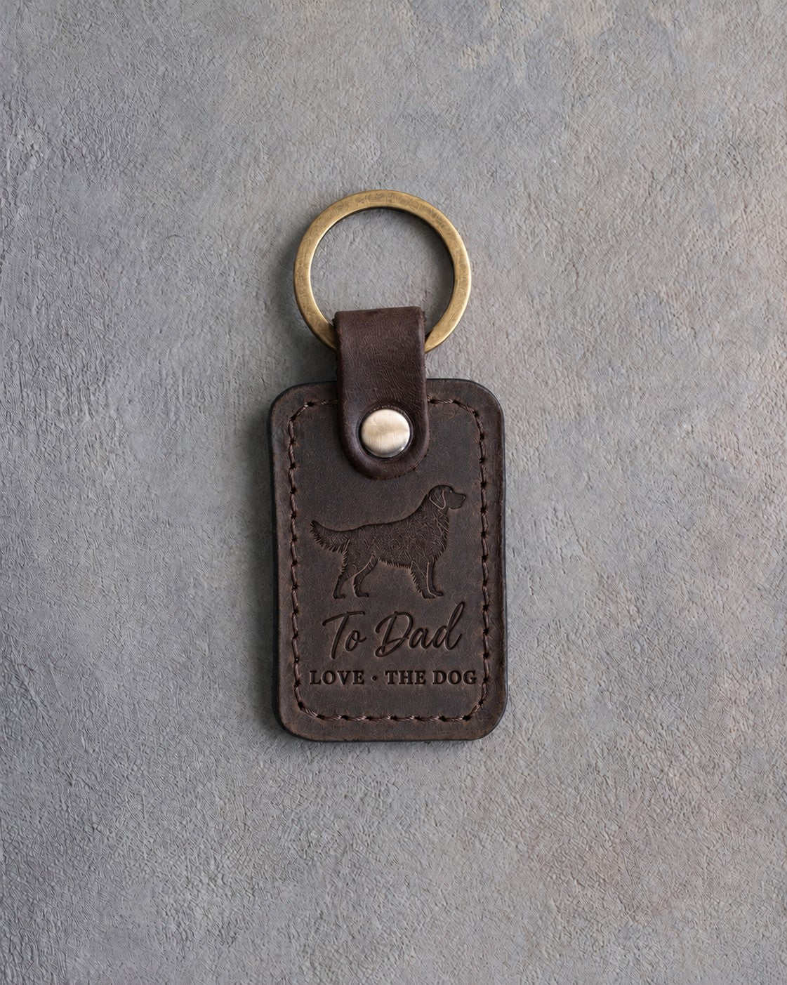 Dark espresso leather keychain debossed with a golden retriever silhouette above To Dad and LOVE · THE DOG, on gray concrete