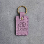 Lilac leather keychain debossed with a curled sleeping dog above To Grandma and LOVE · GRANDDOG, on gray concrete
