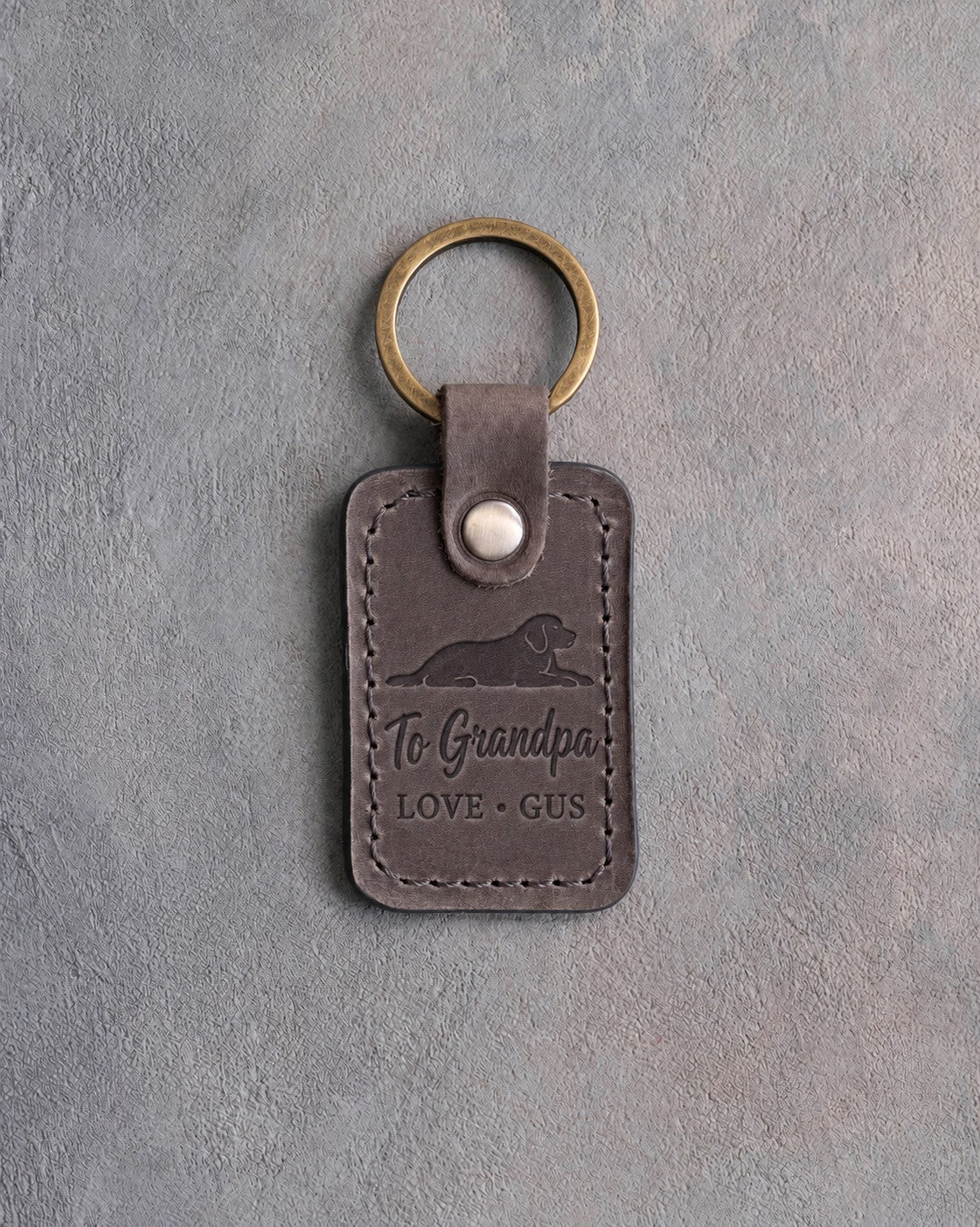 Country gray leather keychain debossed with a dog lying chin on paws above To Grandpa and LOVE · GUS, on gray concrete