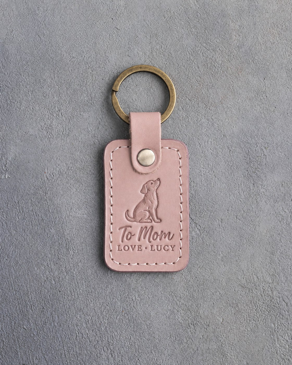 Blush pink leather keychain debossed with a dog looking up above To Mom and LOVE · LUCY, on gray concrete