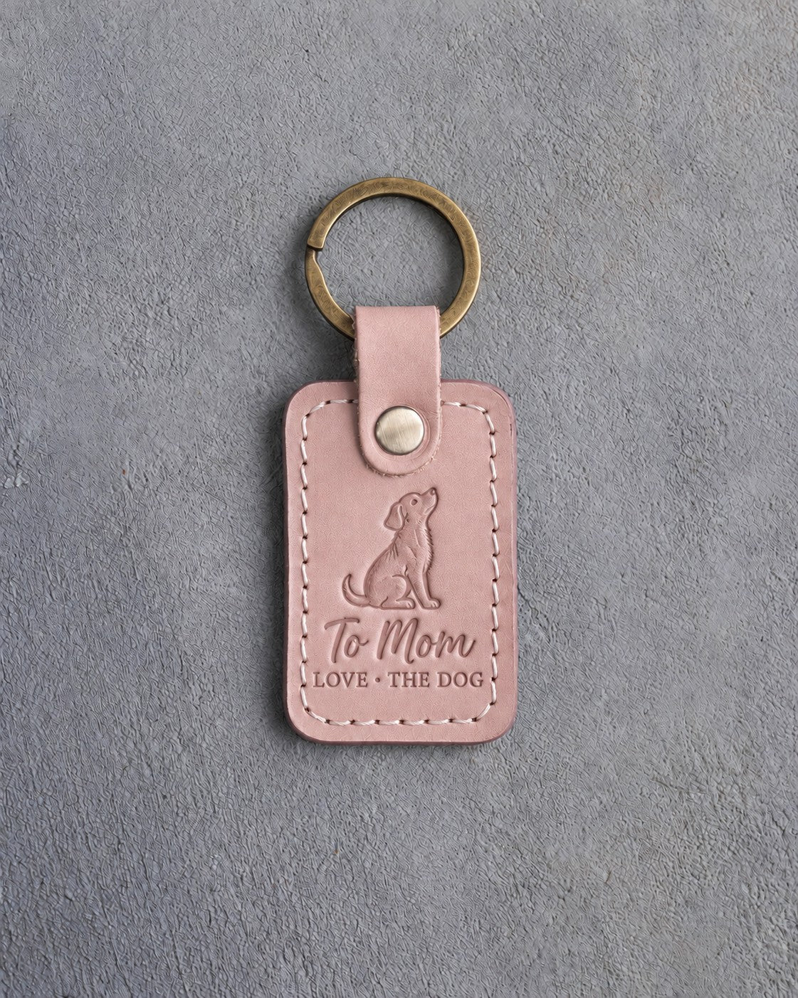 Blush pink leather keychain debossed with a dog looking up above To Mom and LOVE · THE DOG, on gray concrete