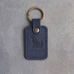 Blueberry navy leather keychain debossed with a sitting dog above TOP OF CLASS, on gray concrete