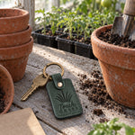 Green Touch Grass keychain lying on a fresh-cut lawn beside a pair of sneakers