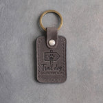 Country gray leather keychain debossed with a trail marker arrow and a paw above the words Trail dog LEADS THE WAY, on gray concrete