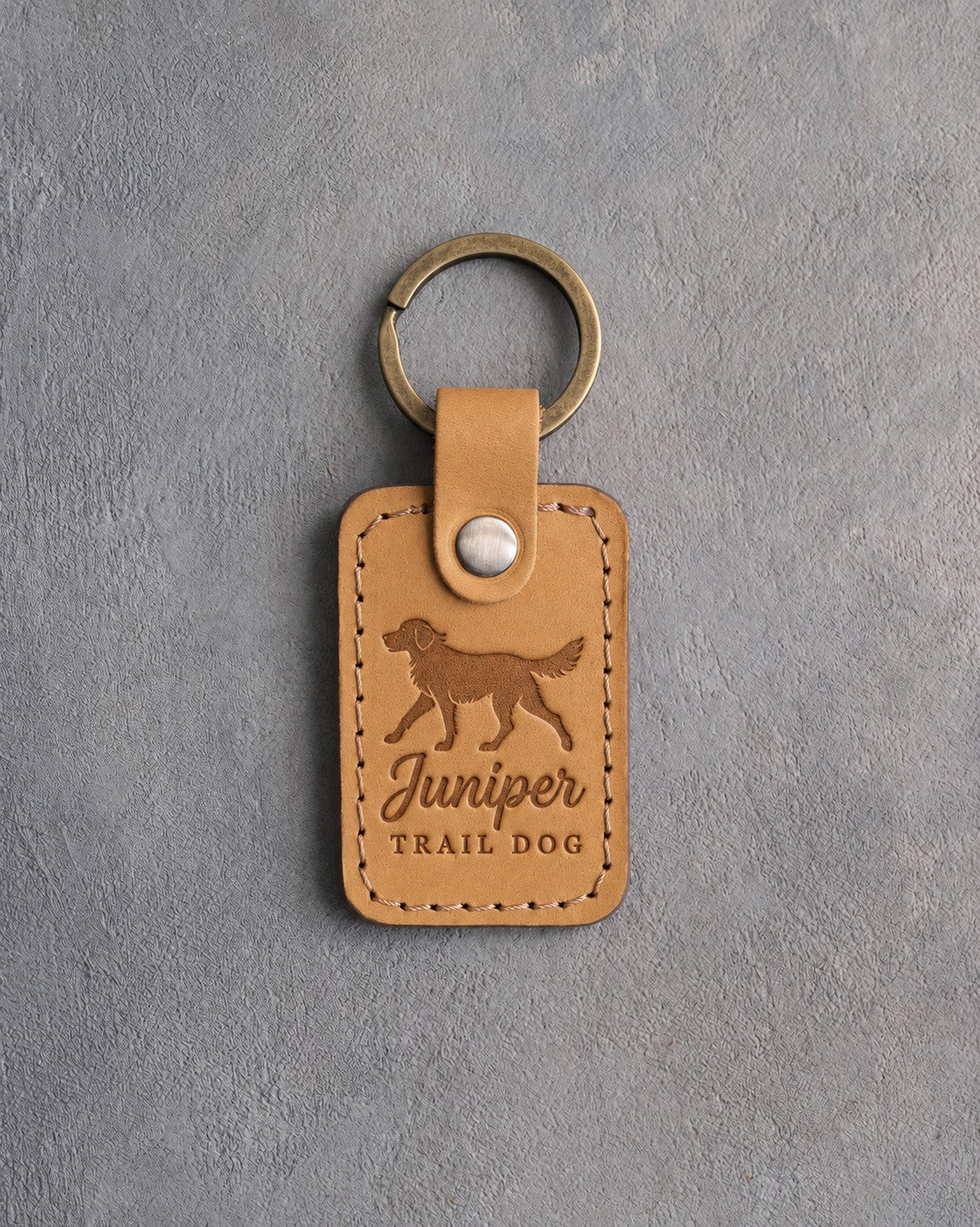 Indian Summer tan leather keychain debossed with a trotting dog above Juniper and TRAIL DOG, on gray concrete