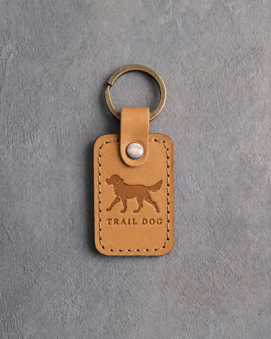 Indian Summer tan leather keychain debossed with a trotting dog above TRAIL DOG, on gray concrete