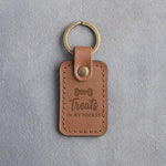 Caramel leather keychain debossed with a bone-shaped dog biscuit and the words Treats IN MY POCKET, on gray concrete