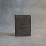 Country gray leather card wallet standing on gray plaster, debossed with a dry fly above Owen and FLY FISHING