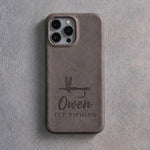 Back of a country gray leather iPhone case debossed with a dry fly above Owen and FLY FISHING below the camera, on gray plaster
