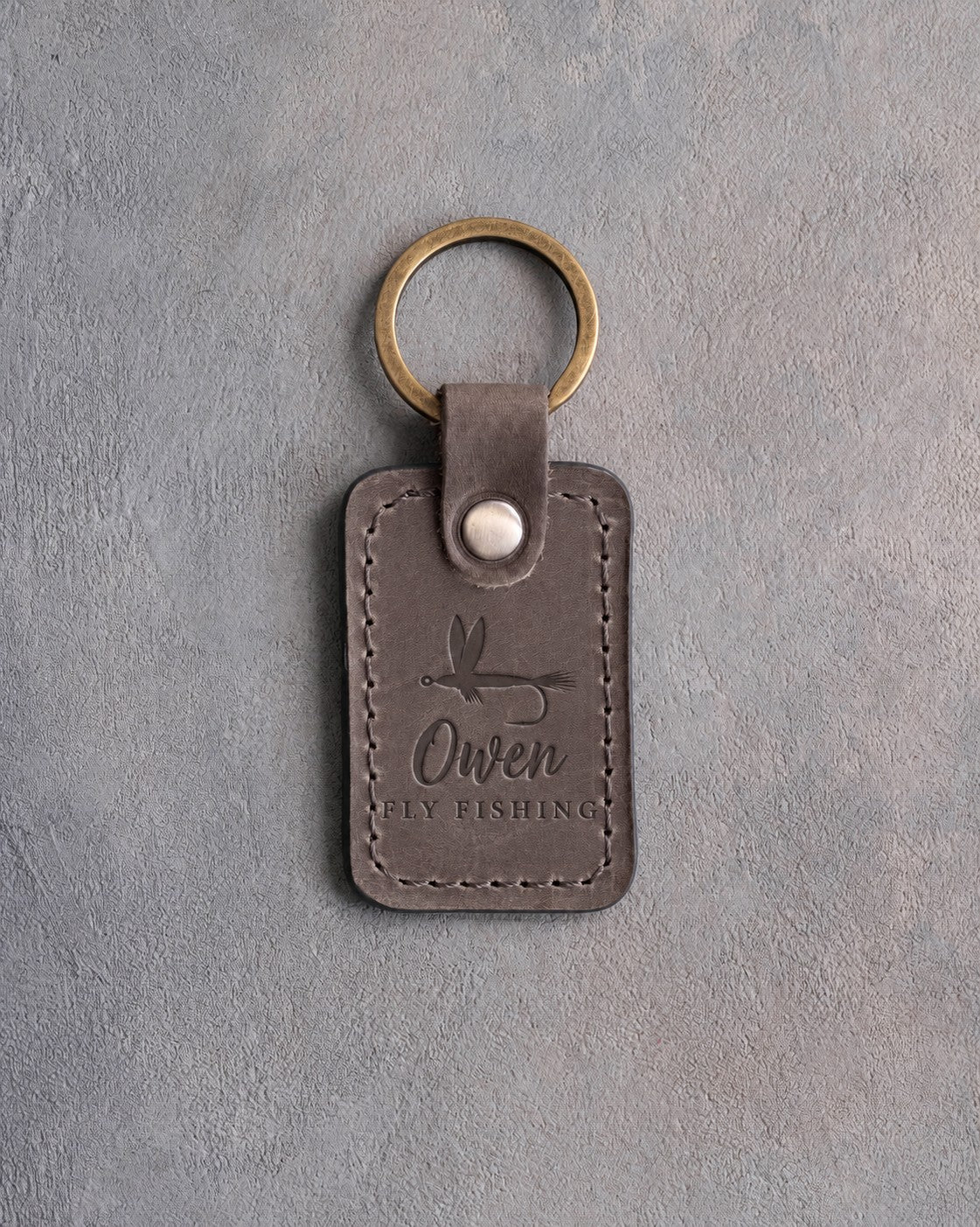 Country gray leather keychain debossed with a dry fly above Owen and FLY FISHING, on gray plaster