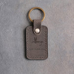 Country gray leather keychain debossed with a dry fly above FLY FISHING, on gray concrete