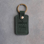 Forest green leather keychain debossed with a rainbow trout above Mike and TROUT, on gray plaster