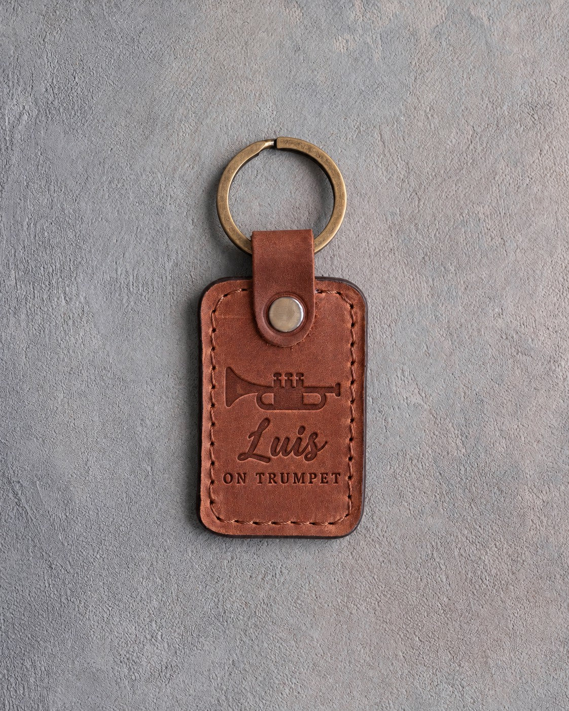 Arizona tan leather keychain debossed with a trumpet above the name Luis and ON TRUMPET, on gray plaster