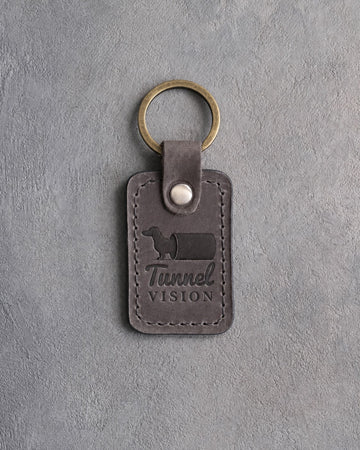 Country gray leather keychain debossed with a dachshund emerging from a tunnel and the words Tunnel VISION, on gray concrete
