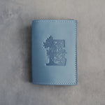 Turquoise leather passport cover with a large floral initial E pressed into the front