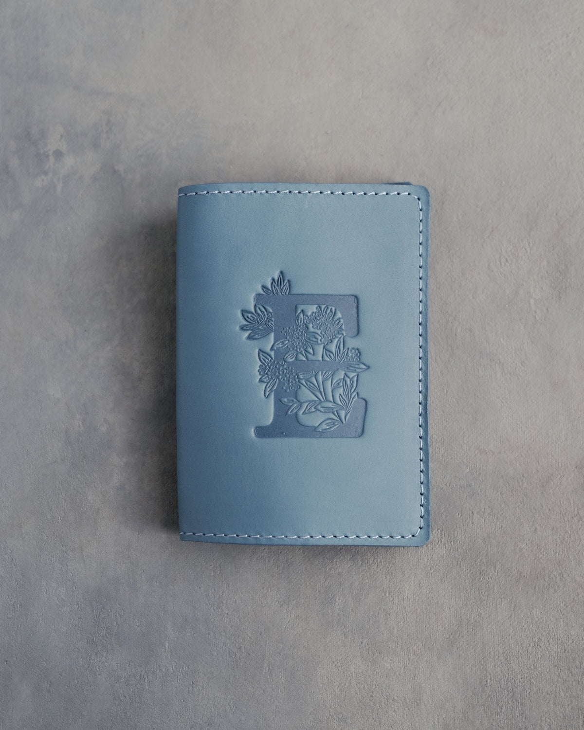 Turquoise leather passport cover with a large floral initial E pressed into the front