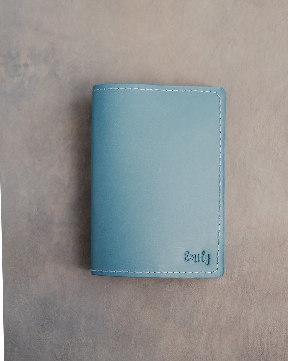 Turquoise leather passport cover with the name Emily in cursive pressed into the bottom corner