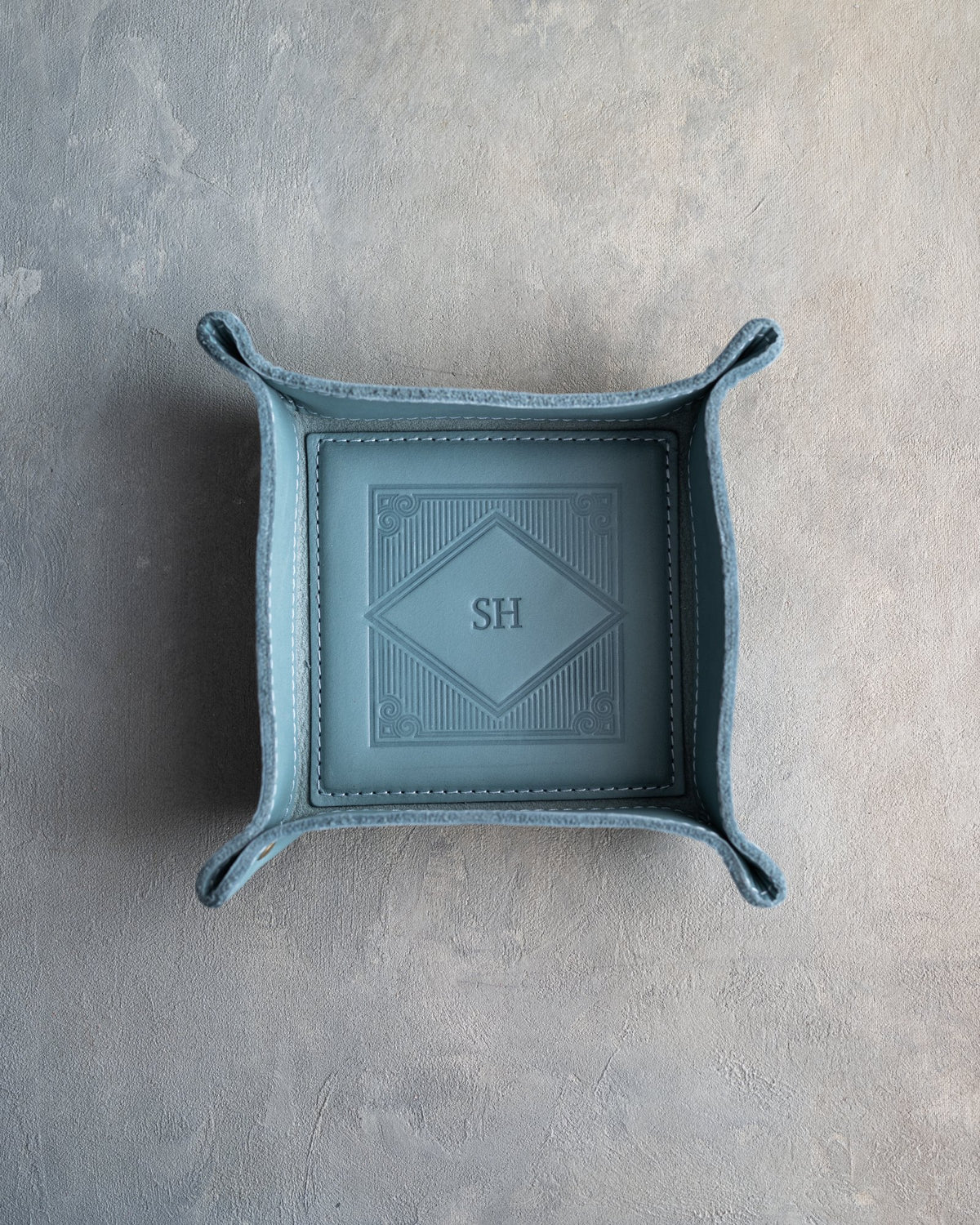 Turquoise leather valet tray with snapped corners and the initials SH pressed into the diamond frame, seen from above