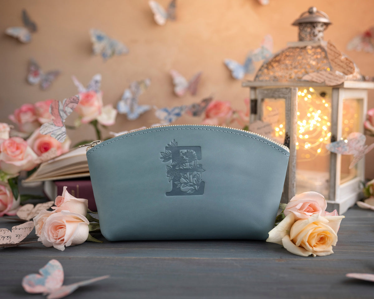 Soft blue leather makeup pouch stamped with a floral letter E, staged with roses and a lantern