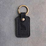 Black leather keychain with a debossed sitting cat above Life with a and TUXEDO CAT, on gray concrete