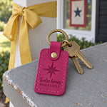 Fuchsia Twelve Homes One Family keychain on a key ring resting on a taped moving box
