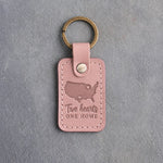 Blush pink leather keychain debossed with a map of the lower forty-eight states and two hearts above Two hearts and ONE HOME, on gray concrete