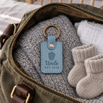 Turquoise Uncle EST 2026 keychain lifted from a small gift box at a family dinner table