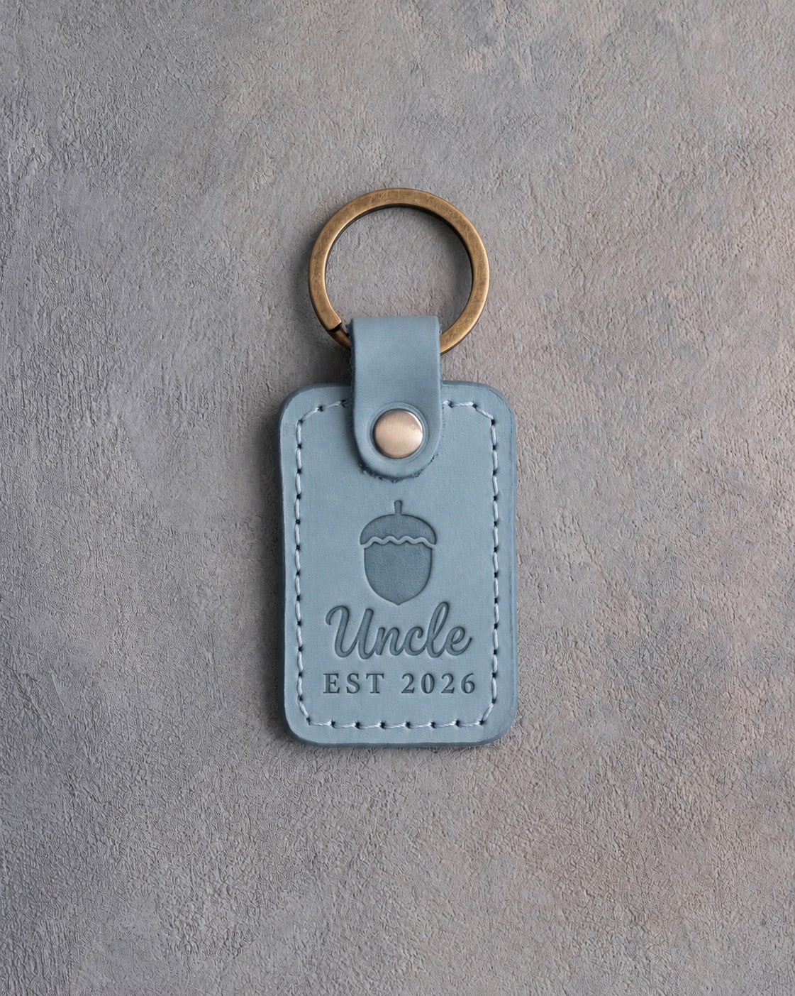 Turquoise leather keychain debossed with a single acorn above Uncle and EST 2026