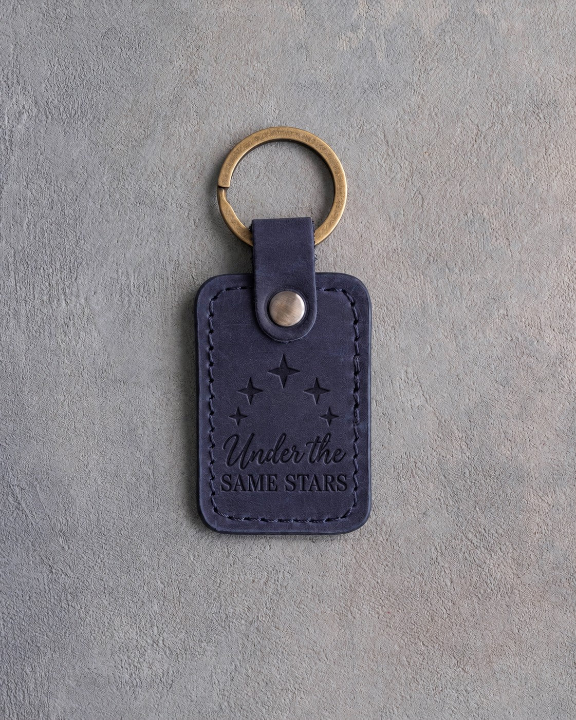 Blueberry navy leather keychain debossed with five bold stars above Under the and SAME STARS, on gray concrete