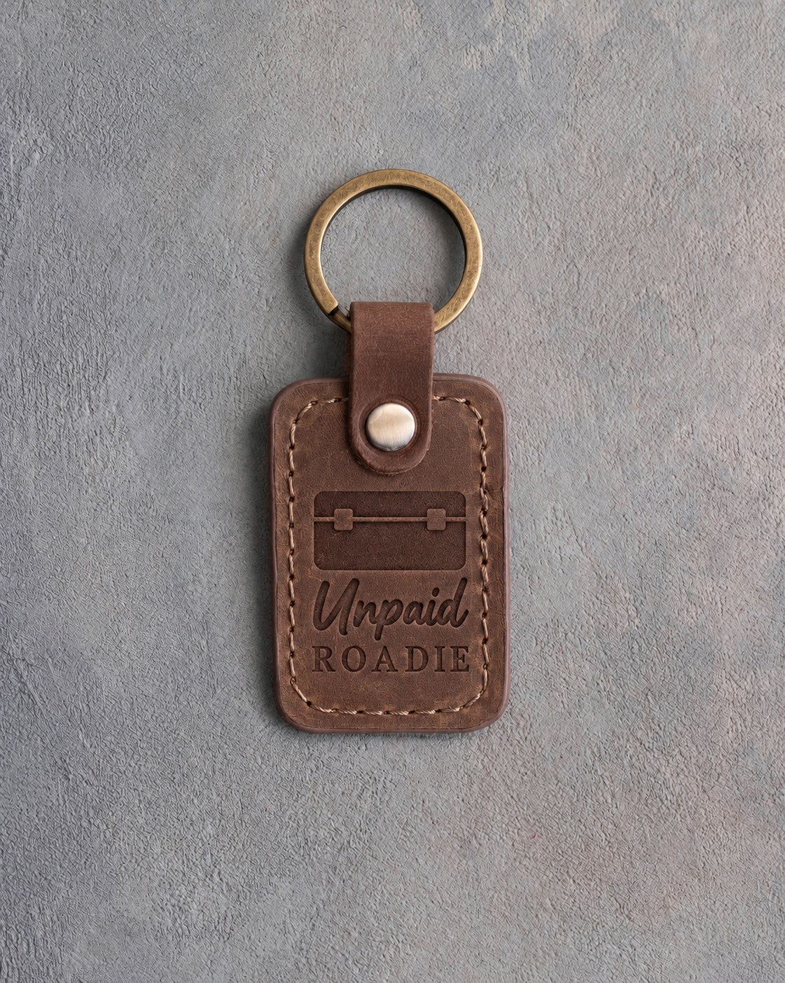 Sicilian brown leather keychain debossed with a road case above the words Unpaid ROADIE, on gray plaster