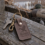 Gray Up Before the Ducks keychain on a key ring beside a headlamp and a travel mug on a dark kitchen counter