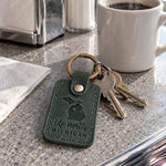 Green Up North Michigan keychain on a cottage key resting on a wooden dock rail over a calm lake
