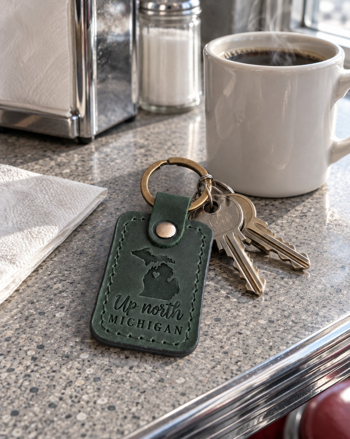 Green Up North Michigan keychain on a cottage key resting on a wooden dock rail over a calm lake