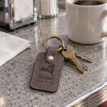 Gray Upstate New York keychain on car keys resting on a snowy windshield wiper in a driveway